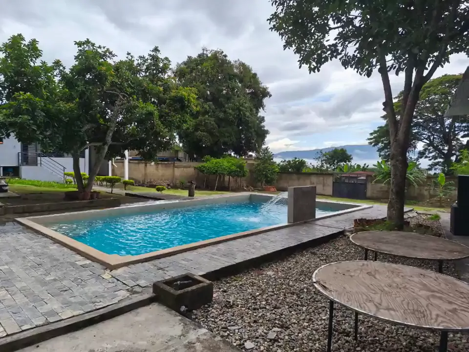 Jardín de La Huerta con árboles grandes, mesas y la piscina al fondo
